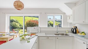 Une cuisine moderne avec des meubles blancs, un grand îlot central et une vue sur un paysage verdoyant par les fenêtres.