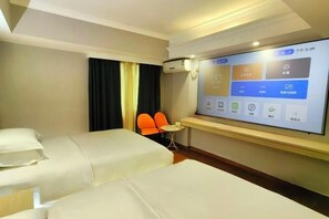 Une chambre d’hôtel avec deux lits, une petite table, une chaise orange et un écran fixé au mur qui affiche les commandes de la chambre.
