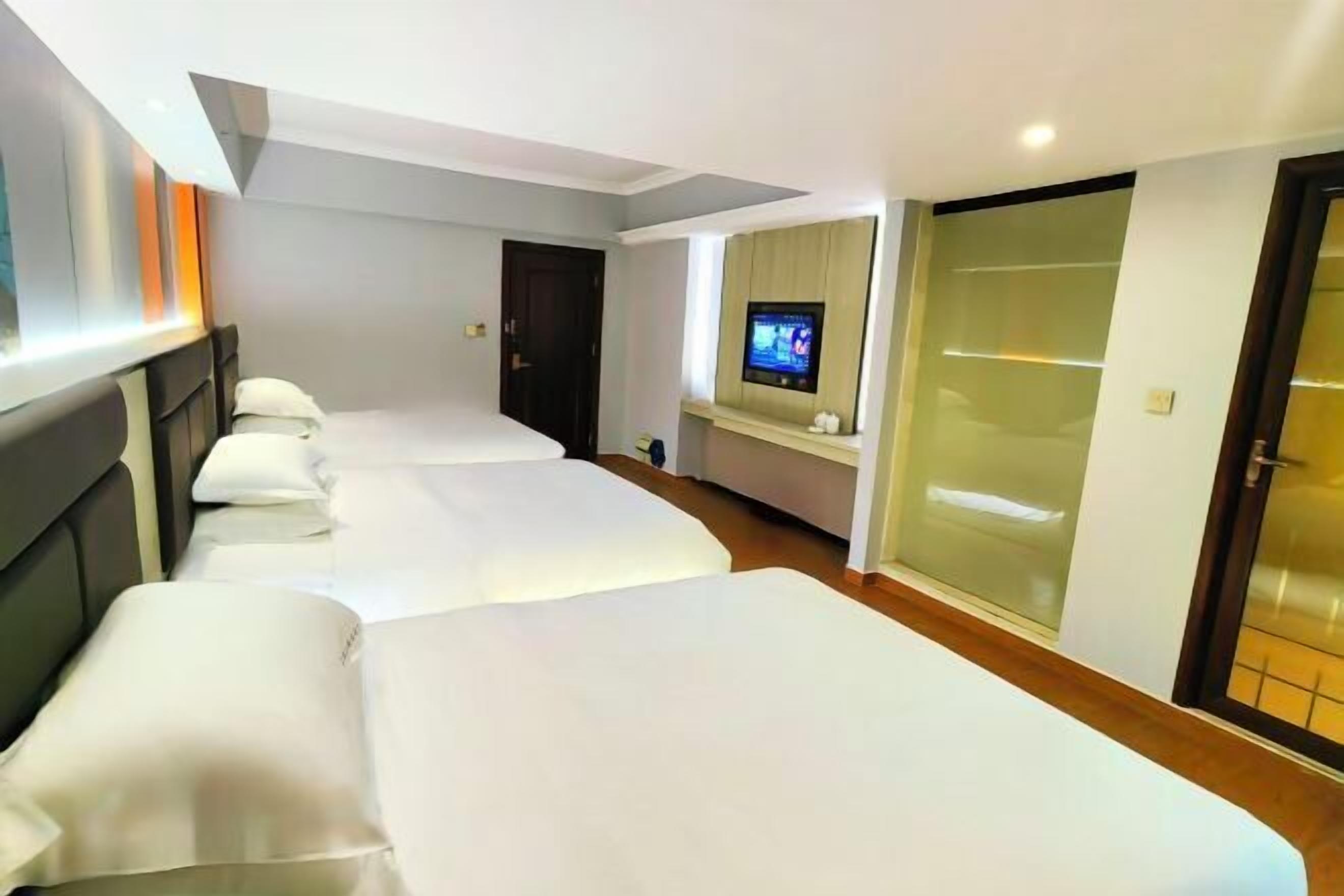 A hotel room with three beds, a television, and a sliding door.