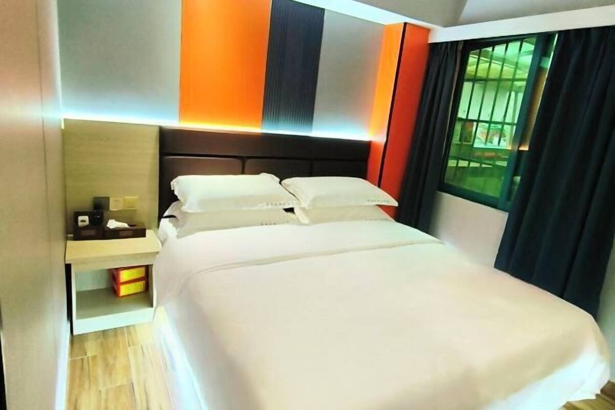 A hotel room with a bed, bedside table, and a window with curtains.