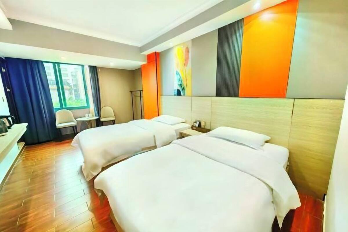 A hotel room with two beds, a desk, a chair, and a large window.