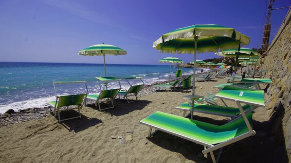 Privat strand, sort sand, solsenger og parasoller