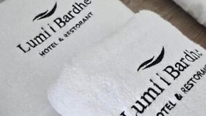 Folded white towels with "Lumi Bardhe Hotel & Restaurant" printed on them.