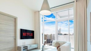 A modern hotel room with a large window, a flat-screen TV, a sofa, and a city view. - LUX The Ultimate Marina View Suite (Dubai)