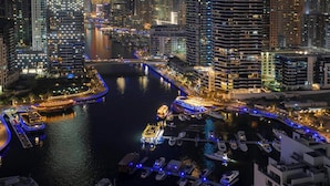 A nighttime cityscape with a river, high-rise buildings, and a marina with boats. - LUX The Ultimate Marina View Suite (Dubai)