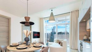 A modern dining area with a round table, chairs, and a city view through large windows. - LUX The Ultimate Marina View Suite (Dubai)