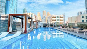 A pool area with lounge chairs and a cabana, surrounded by high-rise buildings. - LUX The Ultimate Marina View Suite (Dubai)