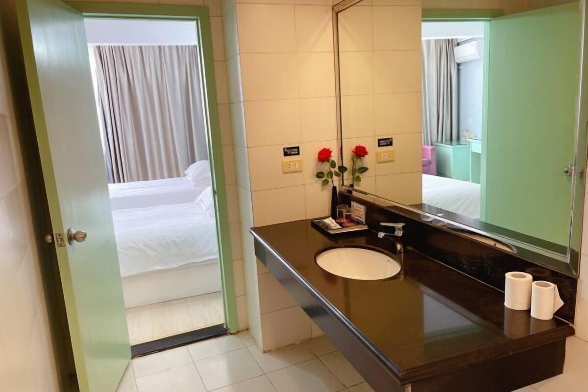 Un baño de hotel con un espejo grande, un lavamanos y una cama visible a través de una puerta abierta.
