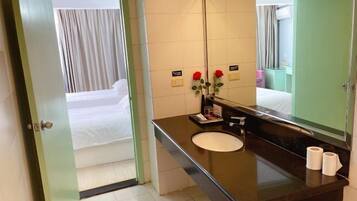 Un baño de hotel con un espejo grande, un lavamanos y una cama visible a través de una puerta abierta.