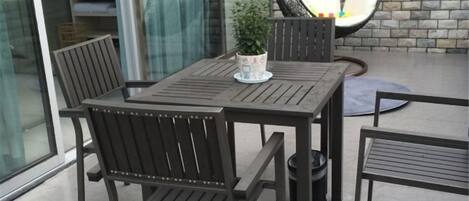 Un espace patio avec une table et des chaises en bois, une plante en pot et un fauteuil suspendu.