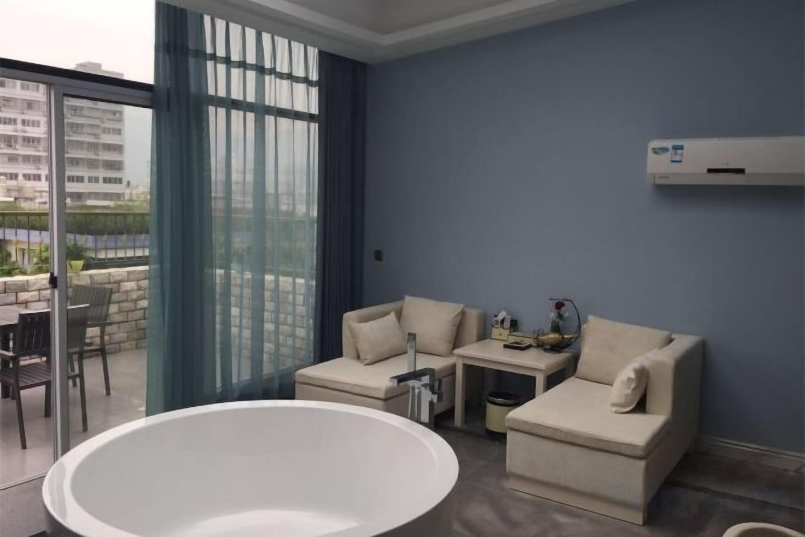 A modern living room with a large bathtub, a sofa set, and a balcony with a view.
