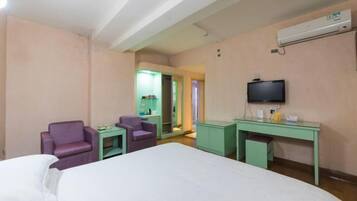 Una habitación de hotel con cama, dos sillas, escritorio, televisión y aire acondicionado.