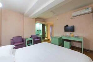 Una habitación de hotel con cama, dos sillas, escritorio, televisión y aire acondicionado.