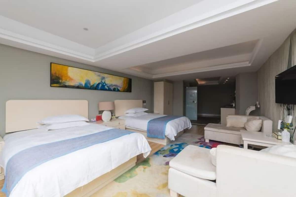 A hotel room with two beds, a sofa, a TV, and a painting on the wall.