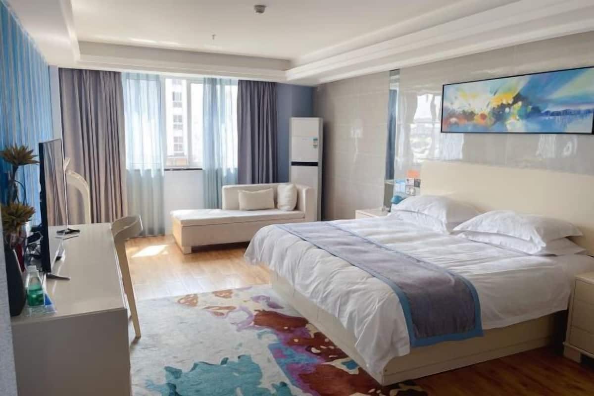 A hotel room with a bed, bedside table, nightstand, desk, chair, and a large window with curtains.
