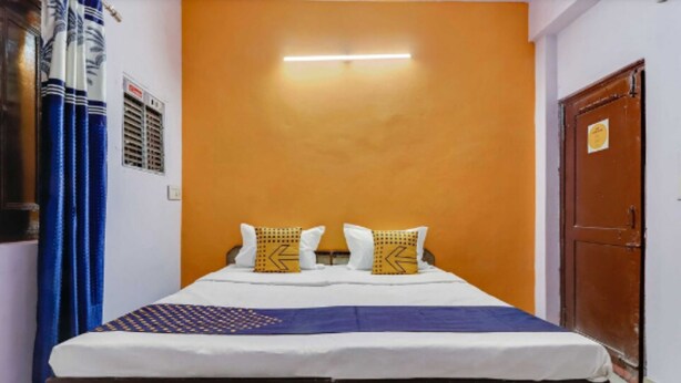 A room with a bed, a blue curtain, an orange wall, and a wooden door. - Bhaskar Hotel By GRB (Ghaziabad)
