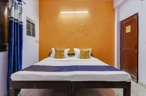 A room with a bed, a blue curtain, an orange wall, and a wooden door. - Bhaskar Hotel By GRB (Ghaziabad)