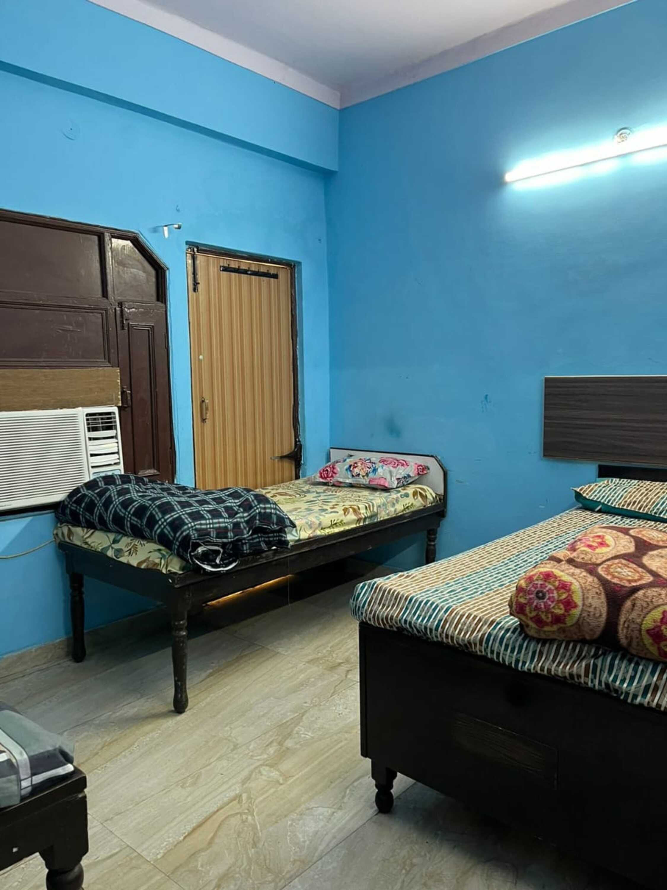 Een kamer met twee bedden, een raam met zonwering, een houten deur en een radiator.