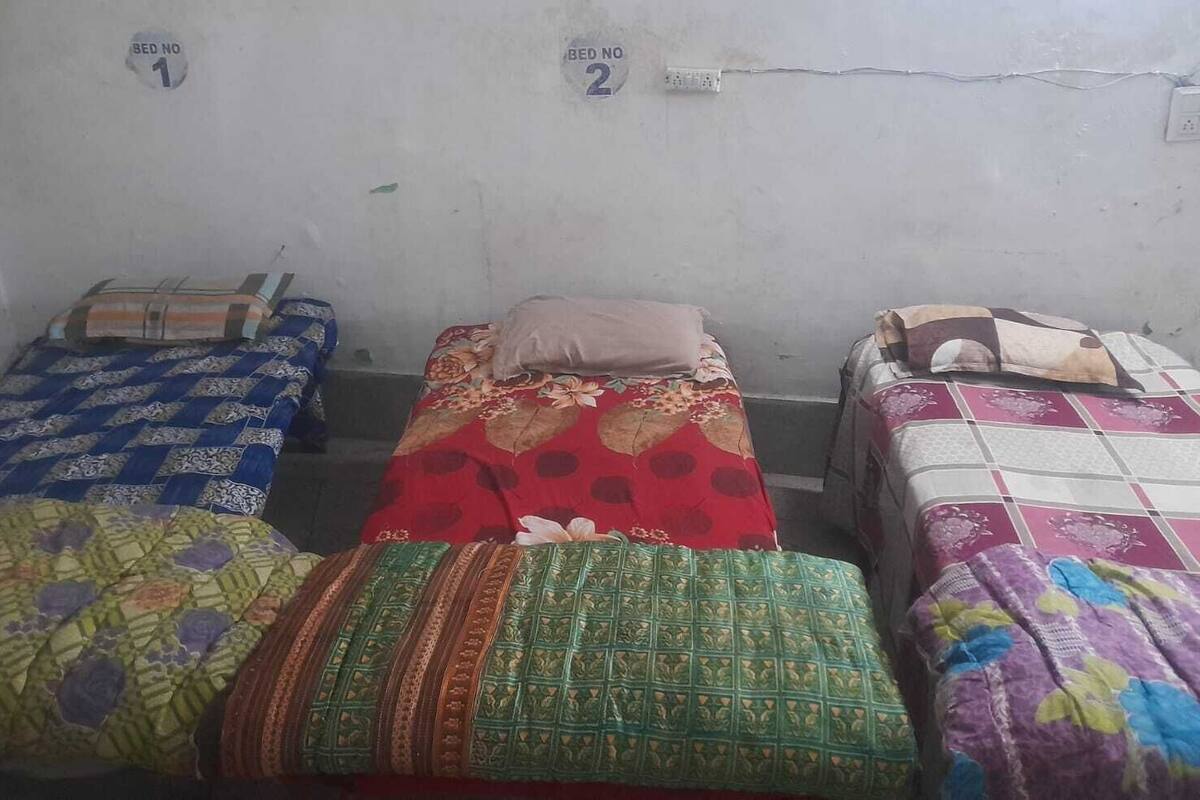 A dormitory room with three beds, each with a distinct patterned bedspread.