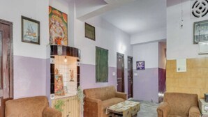 A lobby with two sofas, a small table, and a decorative shelf with religious items. - Bhaskar Hotel By GRB (Ghaziabad)