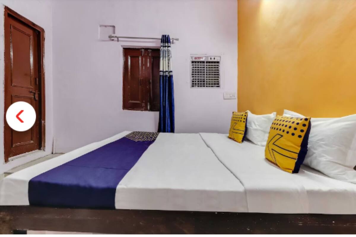 A room with a bed, a window with curtains, a wall-mounted air conditioner, and a door.