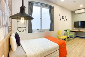 Ein Hotelzimmer mit Bett, Schreibtisch mit Fernseher, Fenster mit Vorhängen und einer Wand-Klimaanlage.