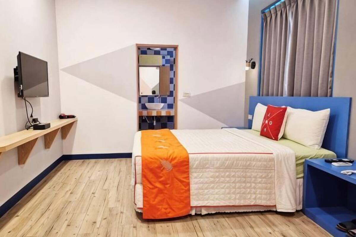 A hotel room with a bed, a TV, a mirror, a sink, and a window with curtains.