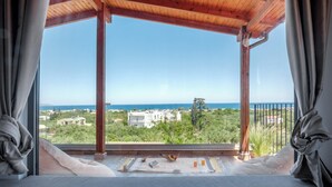 A balcony with a view of the sea and buildings, a wooden ceiling, and a table with a mat, cushions, and a fruit bowl. - Cozy Retreat - Discover tranquility in Maleme, Crete. (GV82+HP2 Maleme, Greece)