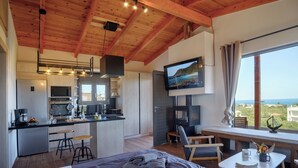 A modern room with a bed, a small table with a cup and a book, a TV, and a kitchen area with stools. - Cozy Retreat - Discover tranquility in Maleme, Crete. (GV82+HP2 Maleme, Greece)