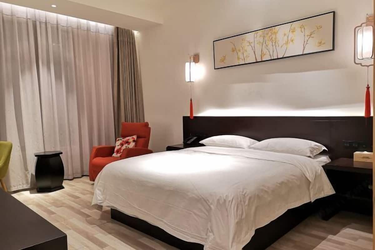 A hotel room with a large bed, a red chair, a nightstand, a lamp, and a painting on the wall.