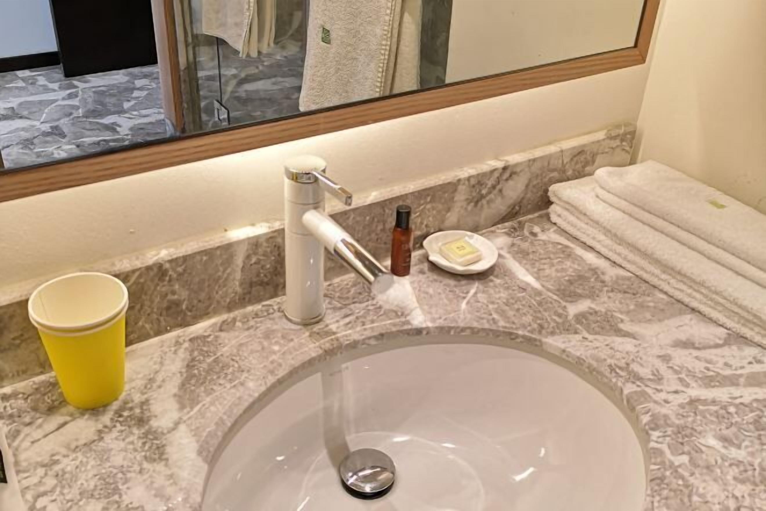 A bathroom with a marble sink, a yellow cup, a soap dish, and a towel stack.