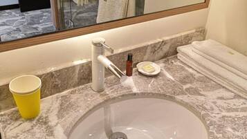 A bathroom with a marble sink, a yellow cup, a soap dish, and a towel stack.