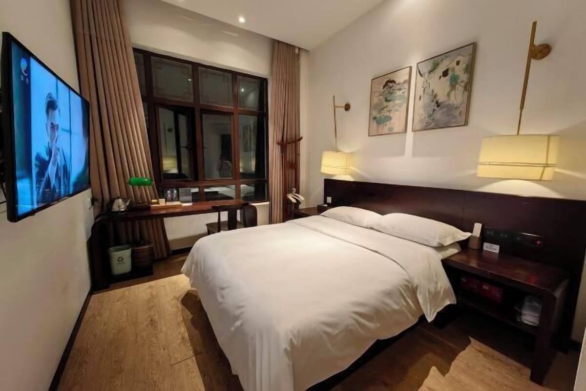 A hotel room with a large bed, a TV, a desk with a lamp, and artwork on the wall.