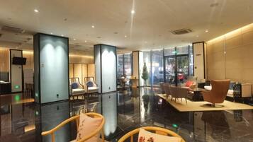 Un hall d’hôtel moderne doté d’espaces de détente, d’un comptoir d’accueil et d’une grande fenêtre donnant sur la rue.