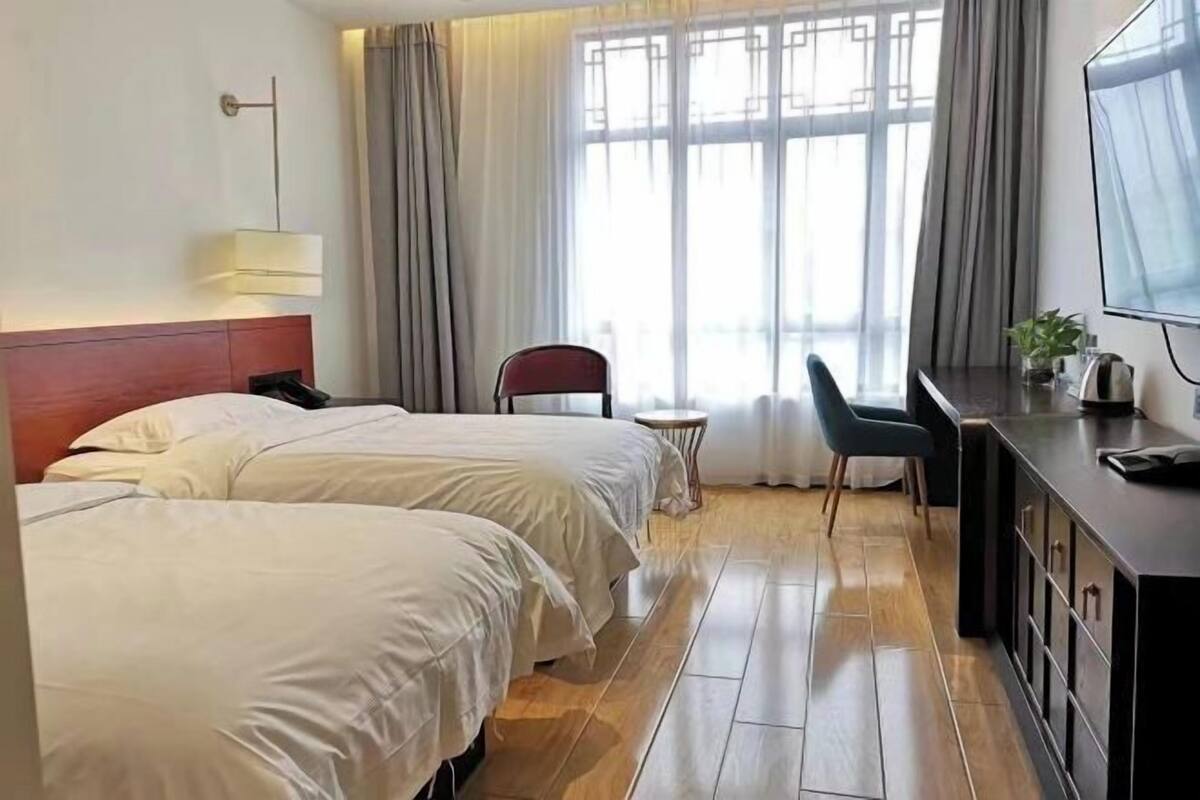 A hotel room with two beds, a desk with a TV, a chair, and a small table.