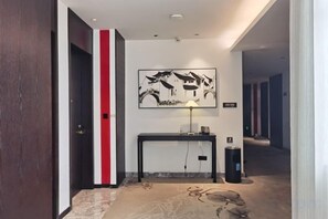 Un couloir avec une bande rouge sur le mur, une console noire sur laquelle est posée une lampe, et une œuvre d’art encadrée au-dessus.
