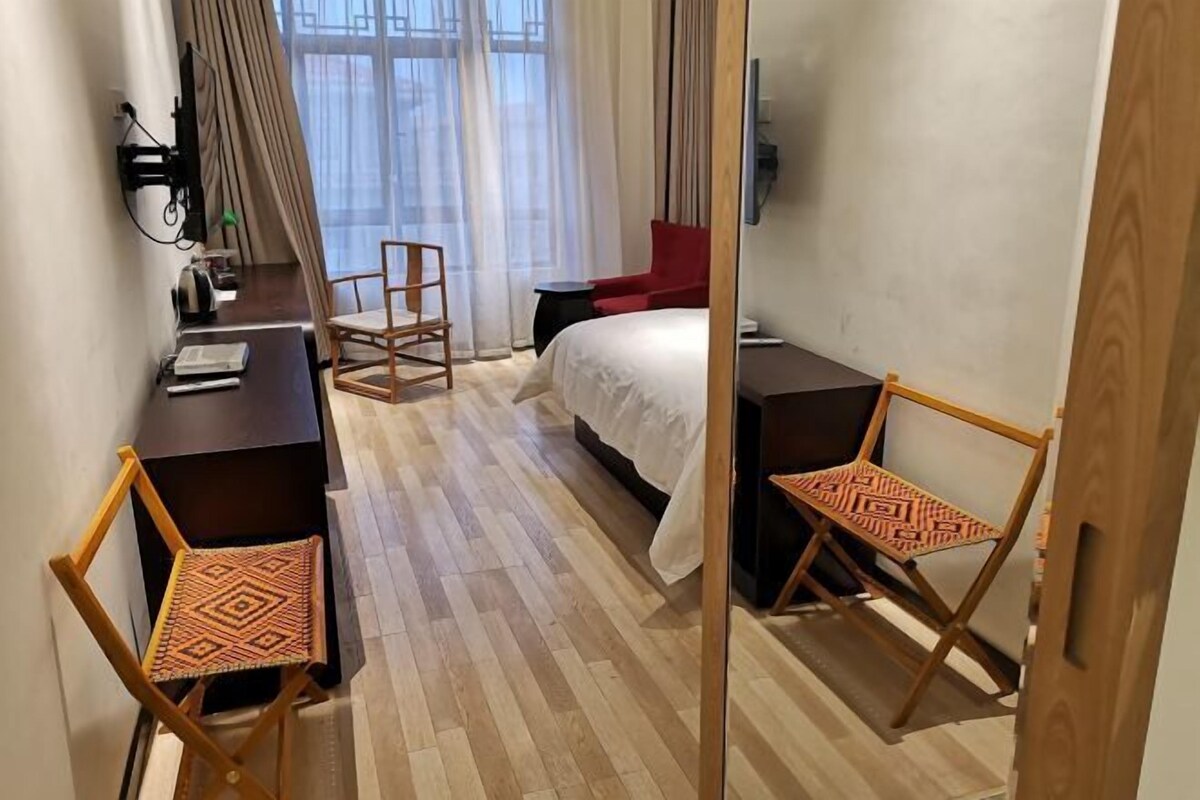 A hotel room with a bed, a desk, two chairs, a TV, and a window with curtains.