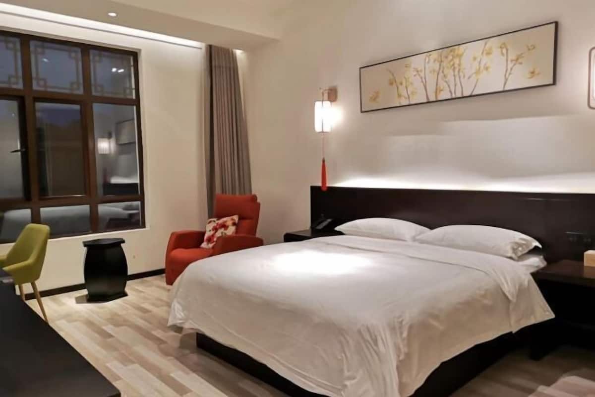 A hotel room with a large bed, a desk, a chair, and a window with curtains.