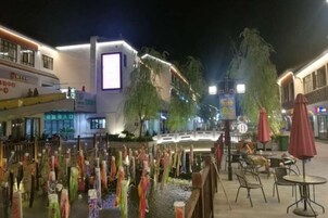 Un espacio exterior para comer con mesas y sillas, una fuente de agua con detalles decorativos y edificios al fondo.