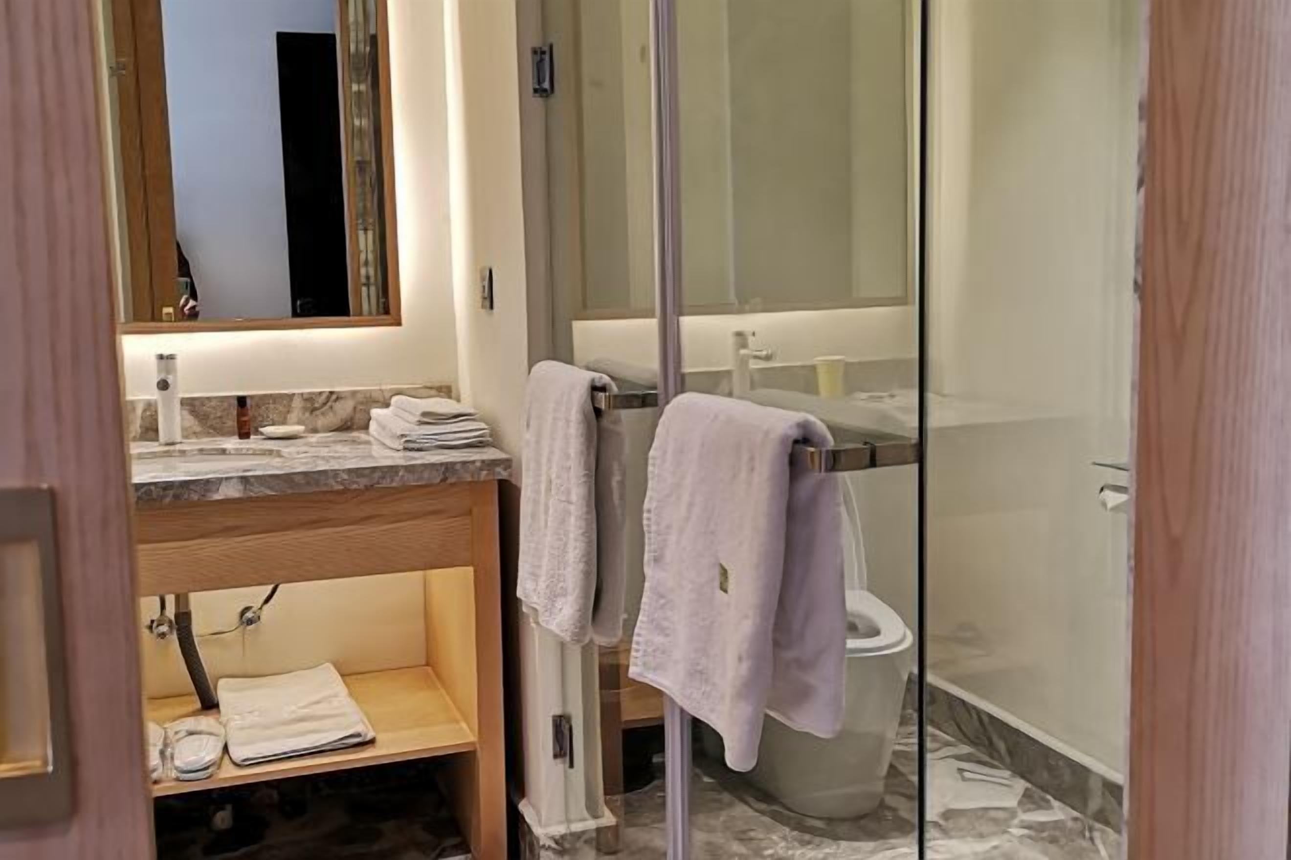 A modern bathroom with a glass shower enclosure, a marble countertop, and a wooden vanity.