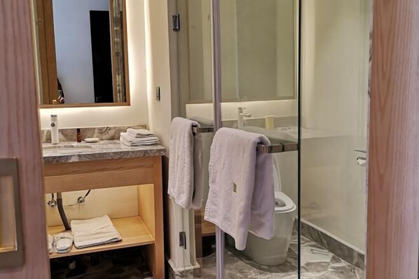 A modern bathroom with a glass shower enclosure, a marble countertop, and a wooden vanity. - Yiwenge Hotel (Changshu)