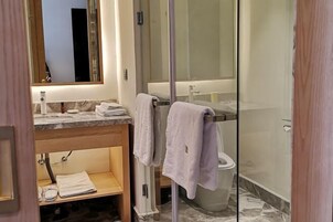 Un baño moderno con cabina de ducha de vidrio, encimera de mármol y mueble de tocador de madera.