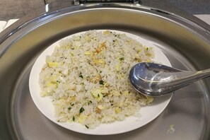 Une assiette de riz frit avec une cuillère, posée sur une table en acier inoxydable.
