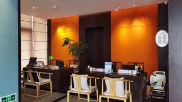 A reception area with a desk, chairs, a plant, and a wall-mounted information board.