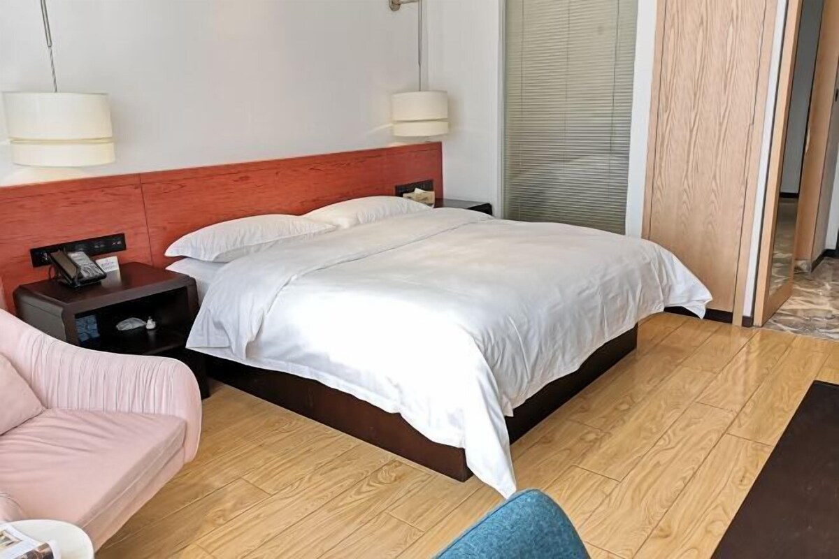 A hotel room with a bed, bedside table, lamp, and a pink sofa.