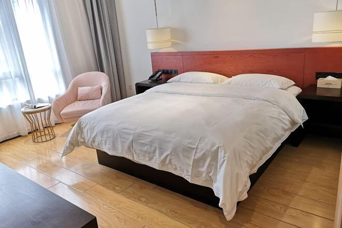 A hotel room with a large bed, a bedside table, a chair, and a lamp.