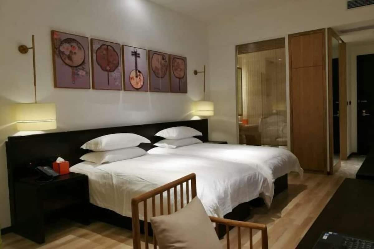 A hotel room with a bed, bedside tables, a chair, artwork on the wall, and a wardrobe.