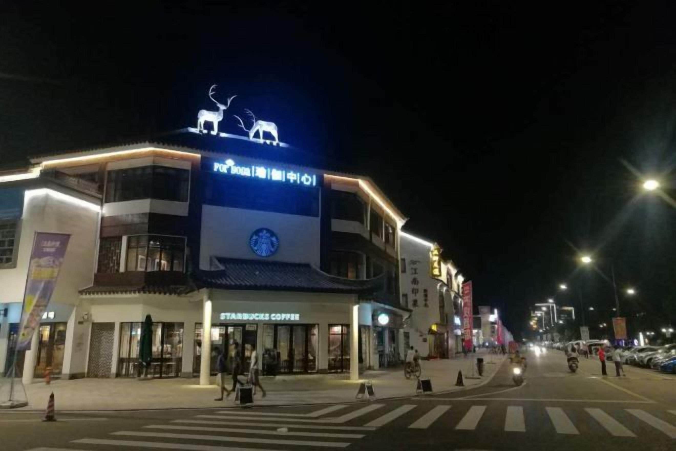 A multi-story building with a Starbucks Coffee shop on the ground floor, a large illuminated sign above the entrance, and a pedestrian crossing in front.