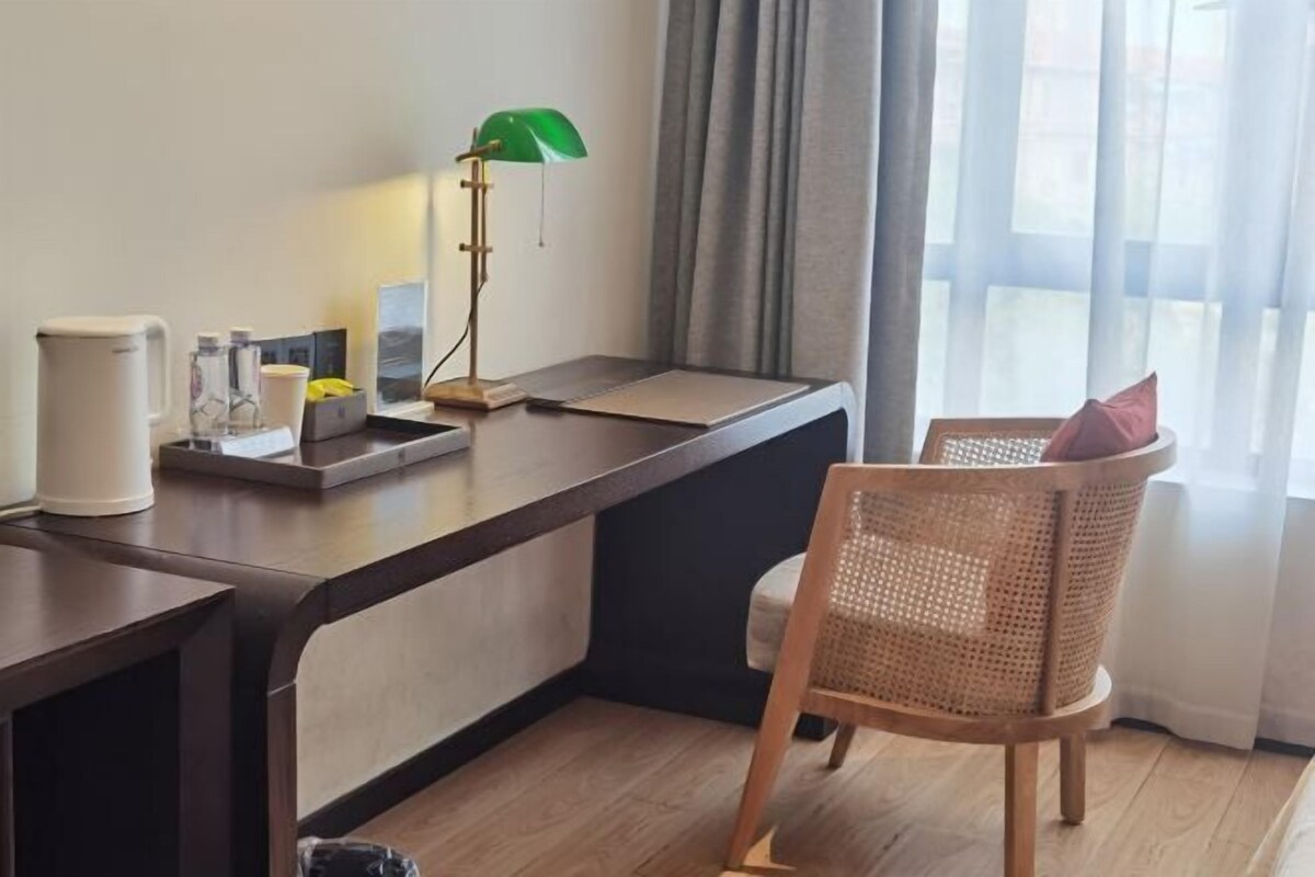 A room with a desk, a chair, a lamp, and a coffee maker.