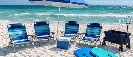 A beach scene with four striped beach chairs, a cooler, a blue paddleboard, and a beach cart.